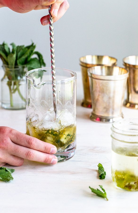 stirring a cocktail in a glass pitcher on a cream background