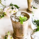 mint julep cocktail with mint garnish on a cream background with flowers