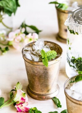 mint julep cocktail with mint garnish on a cream background with flowers
