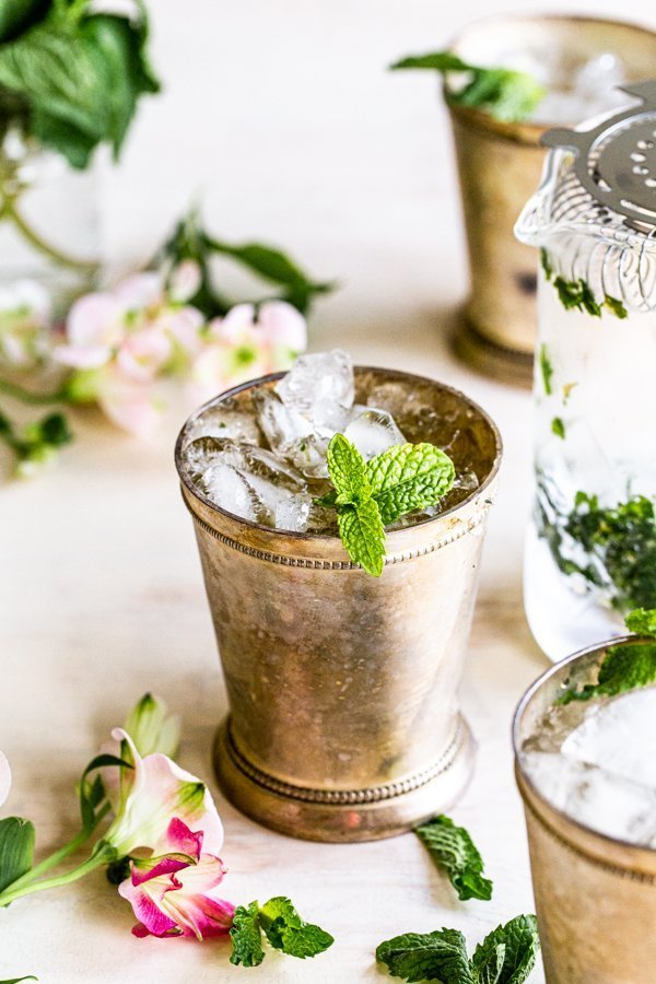 mint julep cocktail with mint garnish on a cream background with flowers