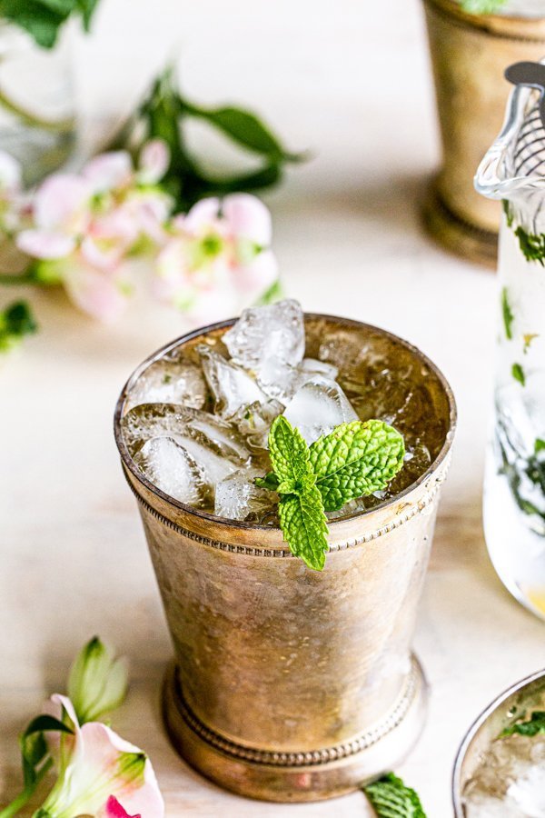 mint julep cocktail with mint garnish on a cream background with flowers