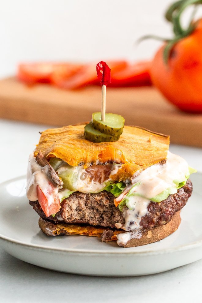 a venison burger with a bite out of it and sweet potato bun on a white small plate