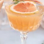 grapefruit cocktail with a grapefruit slice, a shaker cap, herbs on a white background