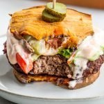 a venison burger with a bite out of it and sweet potato bun on a white small plate