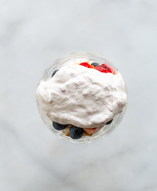 blueberries and strawberries and graham crackers covered with cream in a sundae dish
