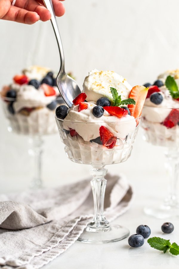berries and cream in a sundae glass with a spoon and a hand