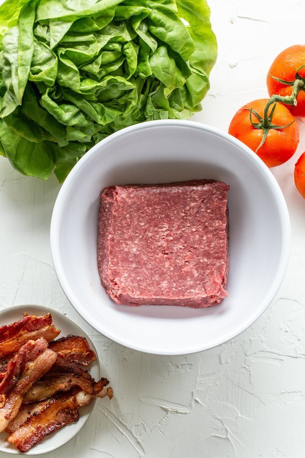 ground meat in a bowl with bacon, lettuce and tomato on a white background