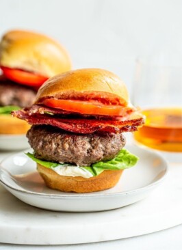 bison burgers on a plate with bacon on them and broubon in the background