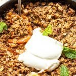 Gluten free peach crisp in a skillet with a dollop of greek yogurt and mint