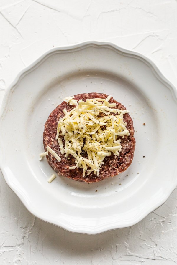 raw elk burger on a white plate with butter in the middle on a white plate