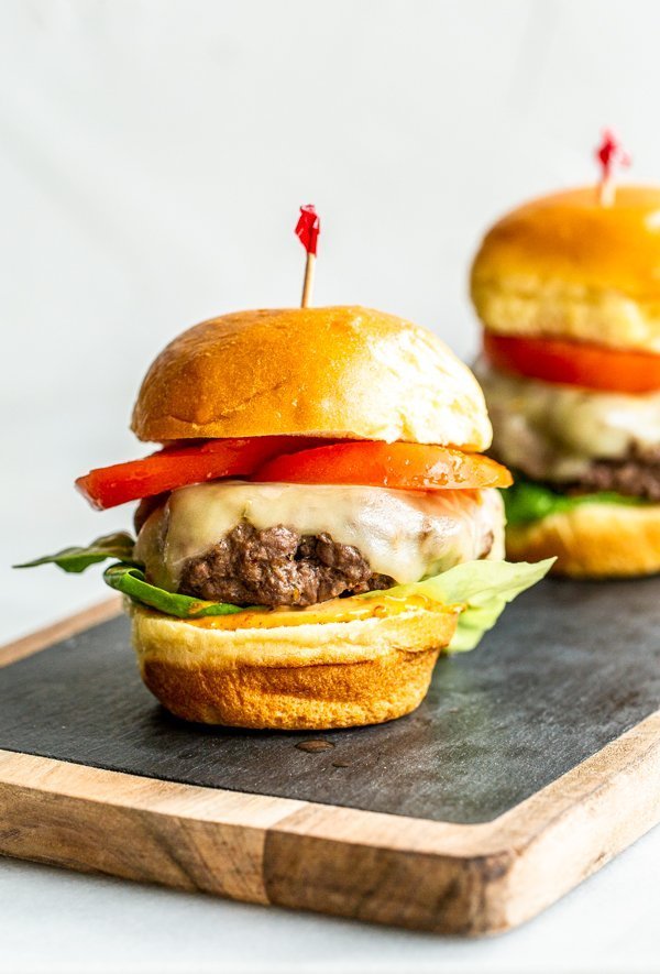 burgers with lettuce, tomato and cheese  made from on a wood and slate board with a white background