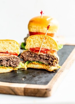 juicy elk burgers with lettuce, tomato and cheese cut in half on a wood and slate board with a white background