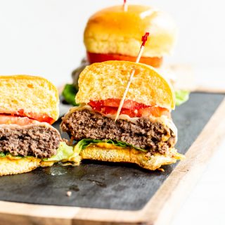 juicy elk burgers with lettuce, tomato and cheese cut in half on a wood and slate board with a white background