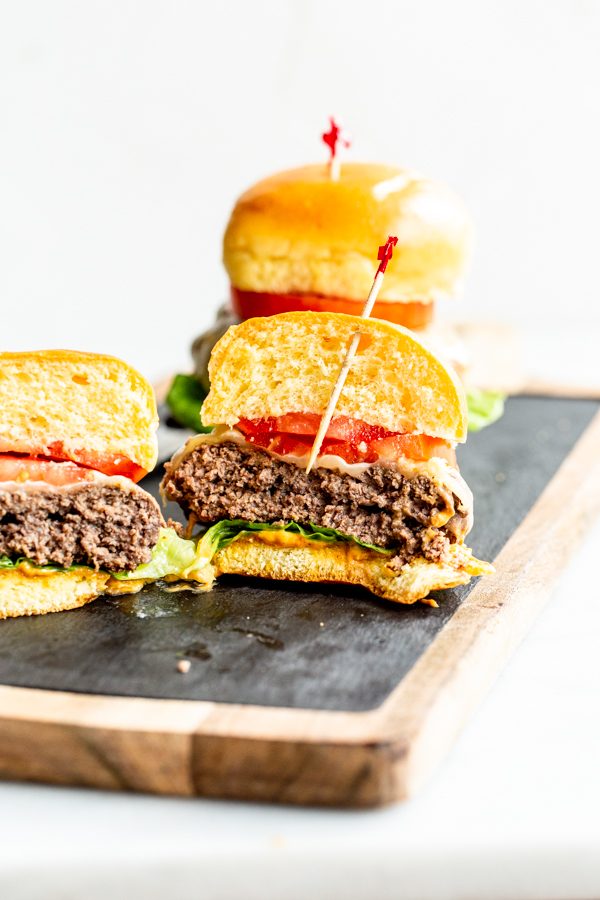 juicy elk burgers with lettuce, tomato and cheese cut in half on a wood and slate board with a white background