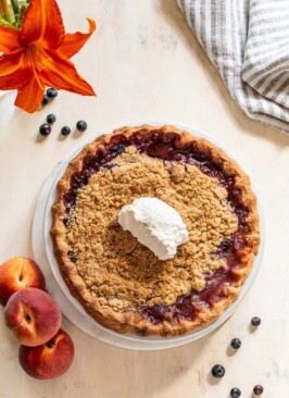 peach blueberry pie with a crumble topping on a cream board with a striped linen napkin
