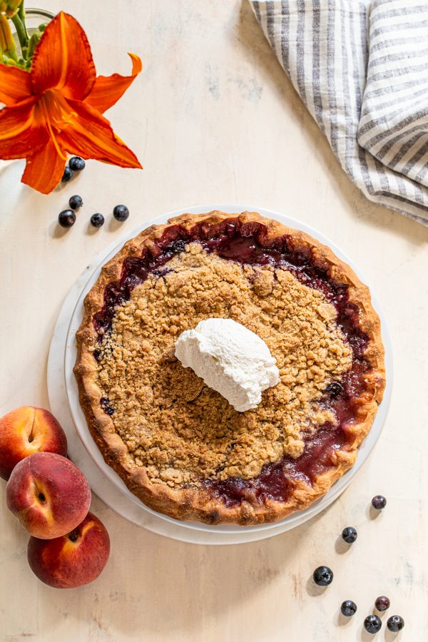 peach blueberry pie with a crumble topping on a cream board with a striped linen napkin