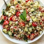 quinoa tabbouleh salad with a mint leaf in a white bowl on a tan background