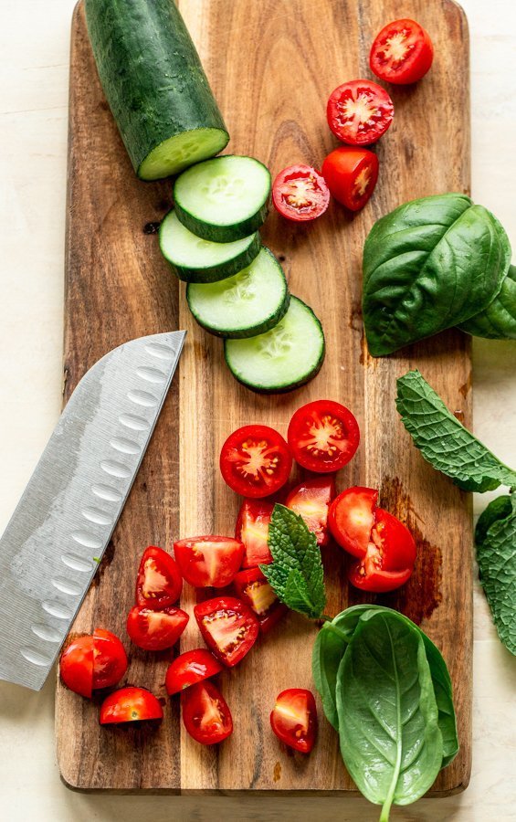 sliced cucumbers and tomato on a wood board with a knife