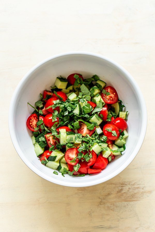 chopped cucumber, basil mint and tomato in a white bowl