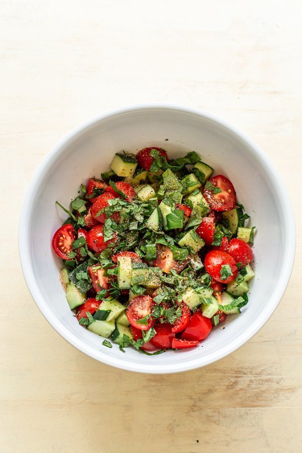 chopped cucumber, basil mint and tomato in a white bowl with dressing