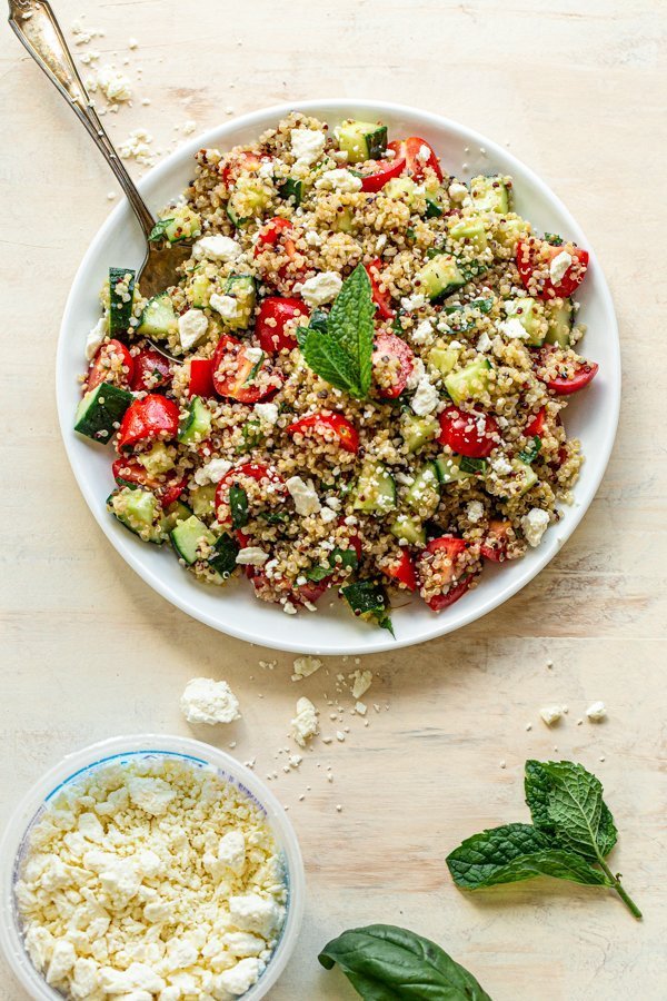 quinoa tabbouleh salad with a mint leaf in a white bowl on a tan background