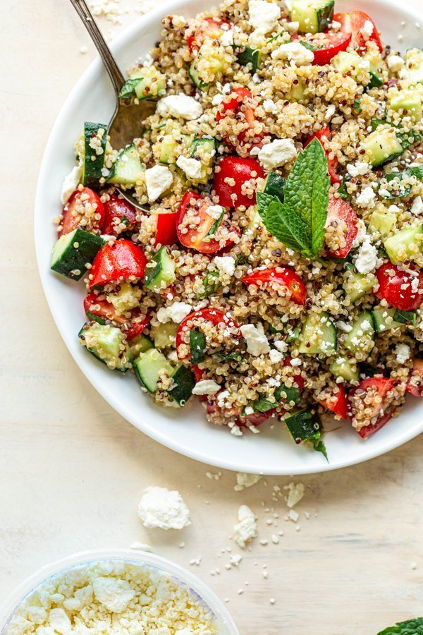 quinoa tabbouleh salad with a mint leaf in a white bowl on a tan background