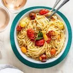 summer pasta with tomatoes and cheese in a white bowl on a blue charger with rosé wine