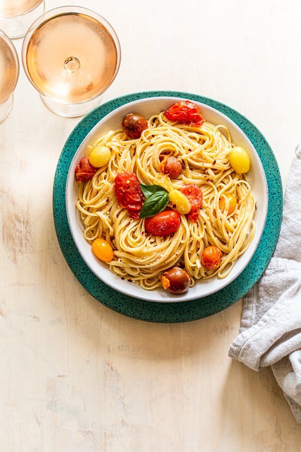 summer pasta with tomatoes and cheese in a white bowl on a blue charger with rosé wine