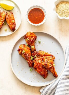 air fryer chicken wings with sweet and spicy wing sauce on a light blue plate with a ramekin of wing sauce and a striped napkin