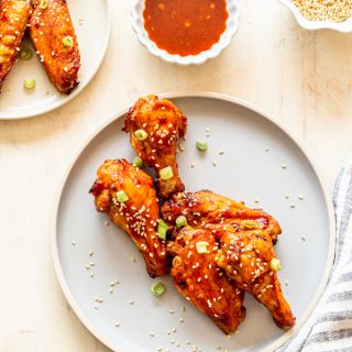 air fryer chicken wings with sweet and spicy wing sauce on a light blue plate with a ramekin of wing sauce and a striped napkin