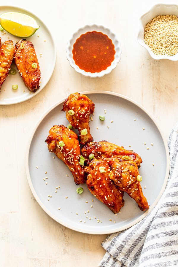 air fryer chicken wings with sweet and spicy wing sauce on a light blue plate with a ramekin of wing sauce and a striped napkin