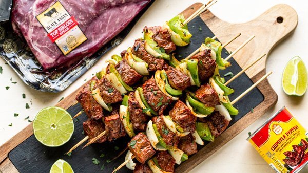 Chipotle steak kabobs with peppers and onions on a cutting board with black slate