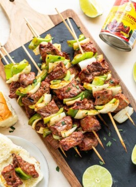 Chipotle steak kabobs with peppers and onions on a cutting board with black slate