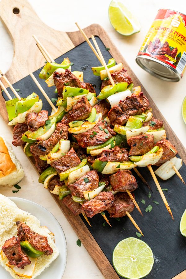 Chipotle steak kabobs with peppers and onions on a cutting board with black slate