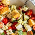 Green Panzanella salad in a white dish with a striped napkin on a wood table