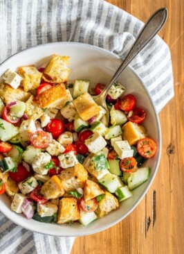 Green Panzanella salad in a white dish with a striped napkin on a wood table