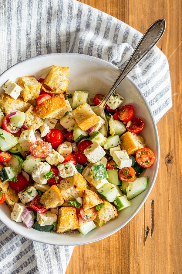 Green Panzanella salad in a white dish with a striped napkin on a wood table