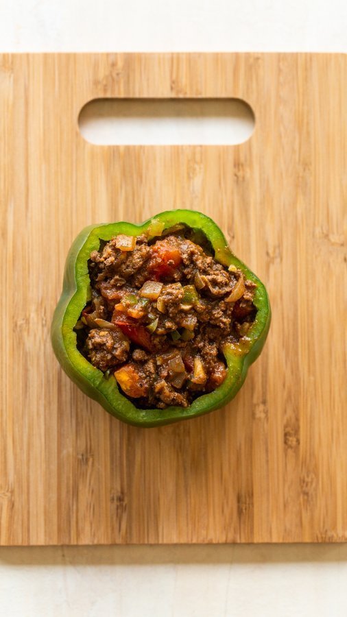 a stuffed pepper, pre cooked on a wood cutting board