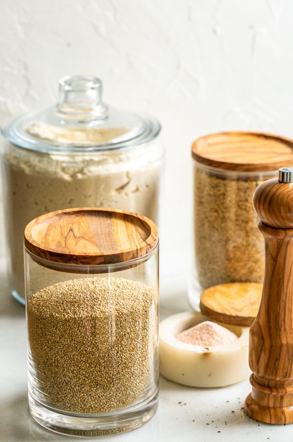 pantry staples bought in bulk in canisters with wood tops on a white counter with white walls