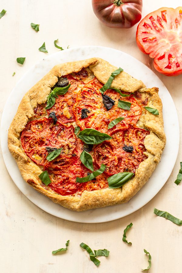 a tomato galette on a marble pastry circle with basil