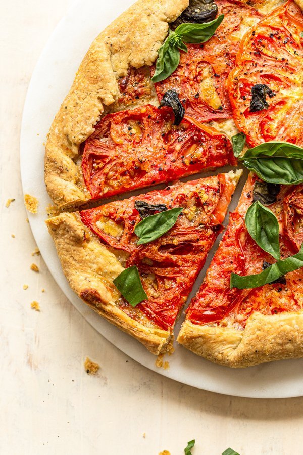 flakey pie crust in a tomato galette with basil and a slice cut out