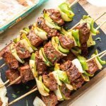 Chipotle steak kabobs with peppers and onions on a cutting board with black slate