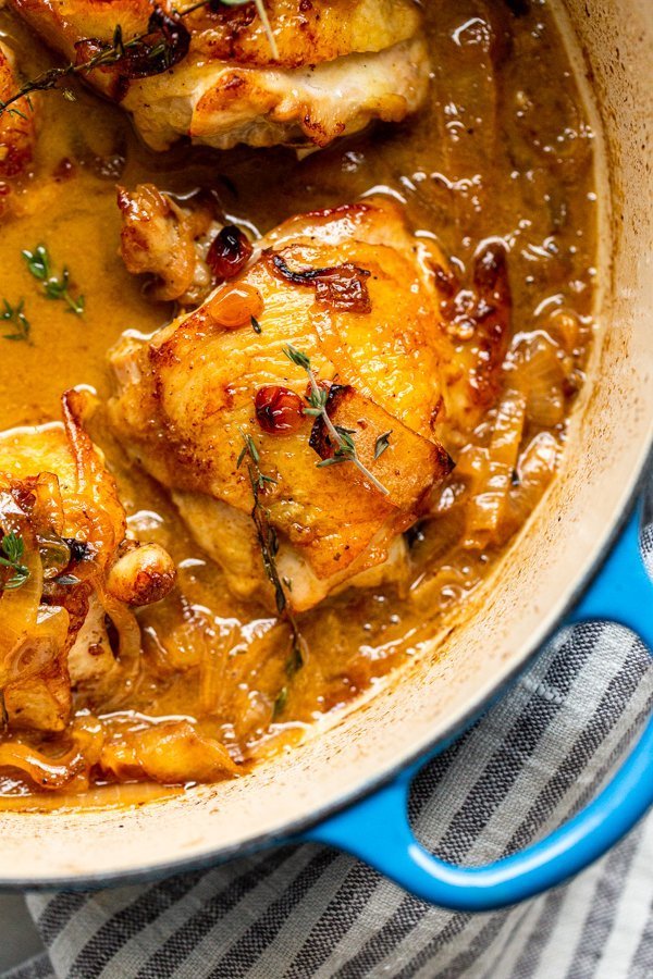 braised apple cider chicken thigh in a dutch oven with golden raisins, thyme, and onions