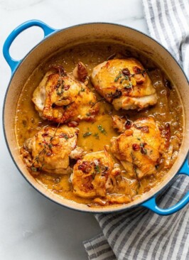 braised apple cider chicken thighs in a dutch oven with golden raisins, thyme, and onions