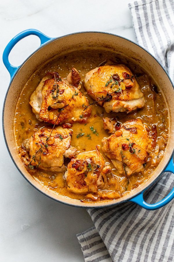 braised apple cider chicken thighs in a dutch oven with golden raisins, thyme, and onions