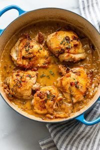 braised apple cider chicken thighs in a dutch oven with golden raisins, thyme, and onions