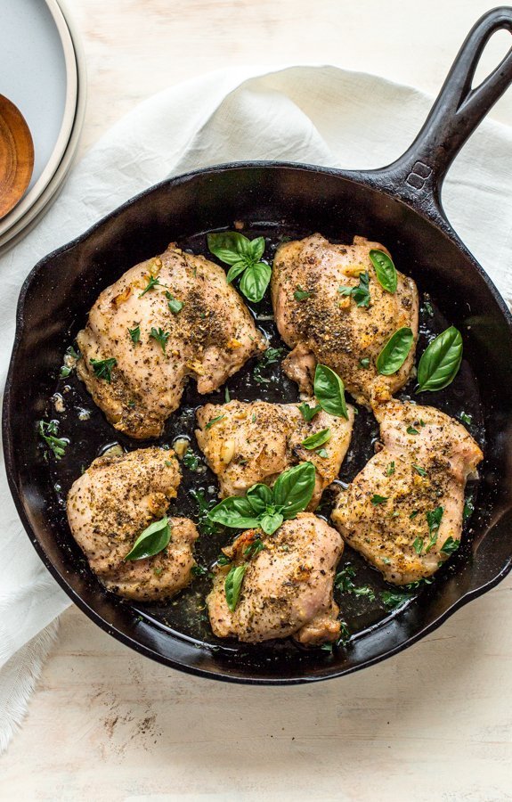 Italian baked chicken thighs in a skillet with basil