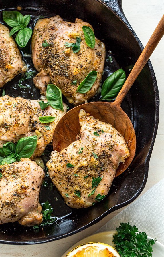 Italian baked chicken thighs in a skillet with a wooden spoon