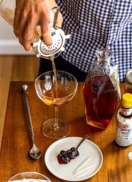 pouring a manhattan cocktail from a cocktail pitcher