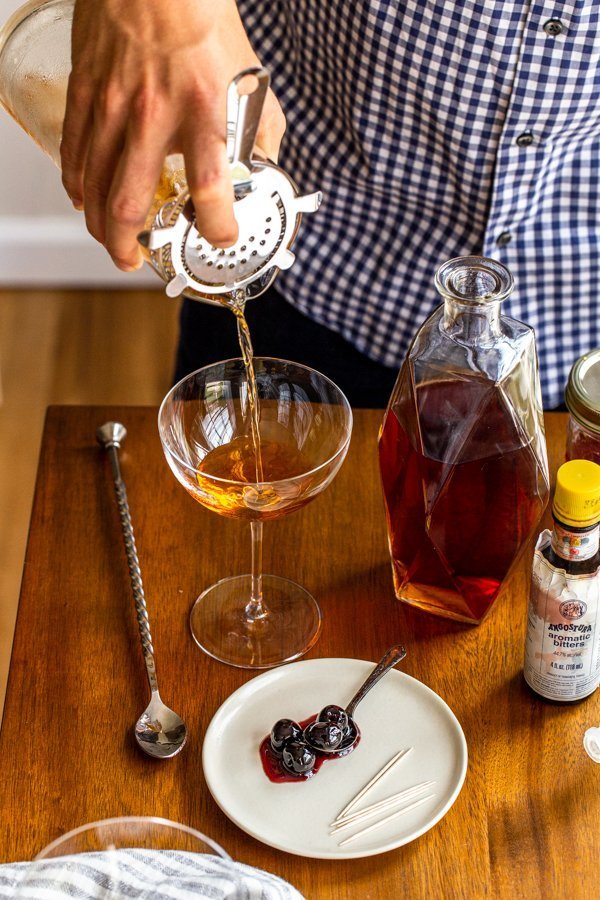 pouring a manhattan cocktail from a cocktail pitcher